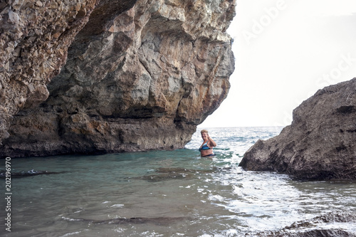A woman swimming near a huge rock at seashore