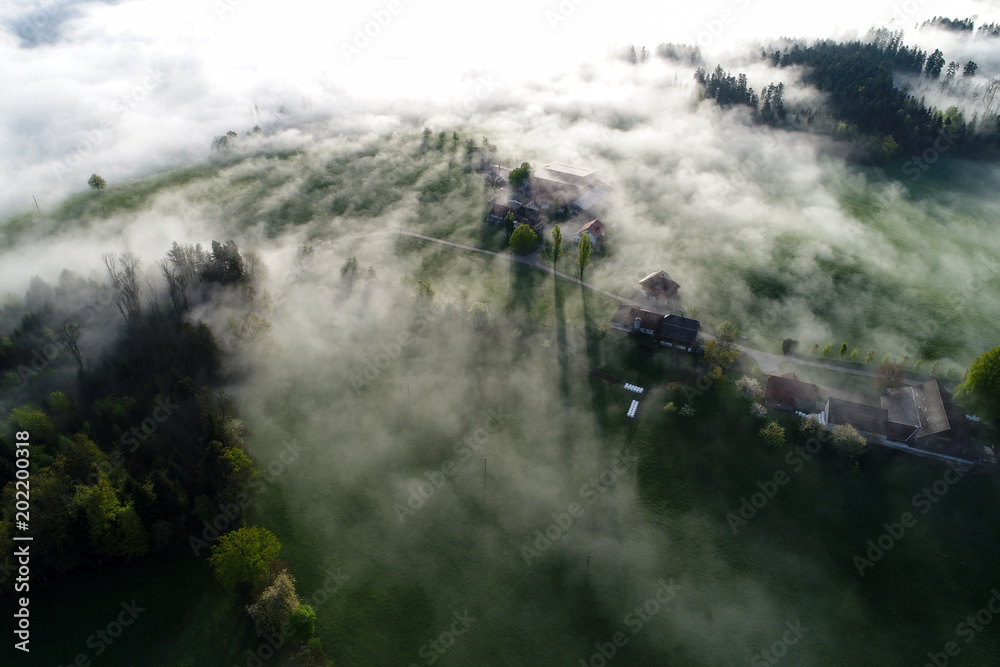 Aerial view Fog clouds pulling through a farm on a spring morning in Switzerland