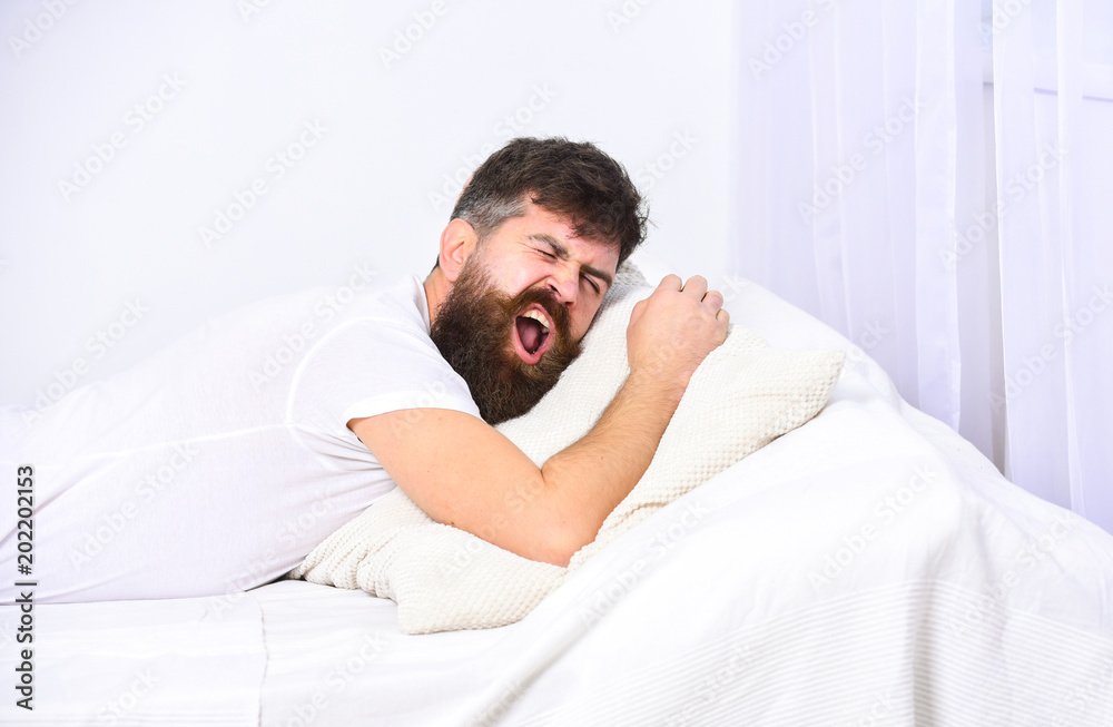 Man in shirt laying on bed, white wall on background. Nap and siesta concept. Guy on sleepy tired face yawning. Macho with beard and mustache yawning, relaxing, having nap, rest. Man in shirt laying on bed, white wall on background. Nap and siesta concept. Guy on sleepy tired face yawning. Macho with beard and mustache yawning, relaxing, having nap, rest.