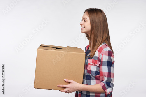 Delivery, relocation and unpacking. Side view portrait of woman holding cardboard box looking forward at blank copy space, isolated