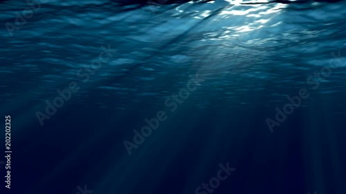 Dark blue sea surface seen from underwater. 
Abstract waves underwater and rays of sunlight shining through. 
