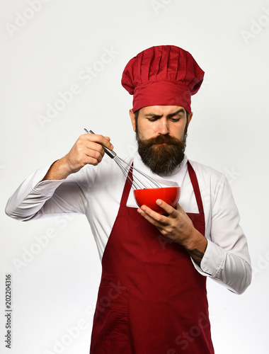 Cook with serious face in uniform uses whisk and bowl