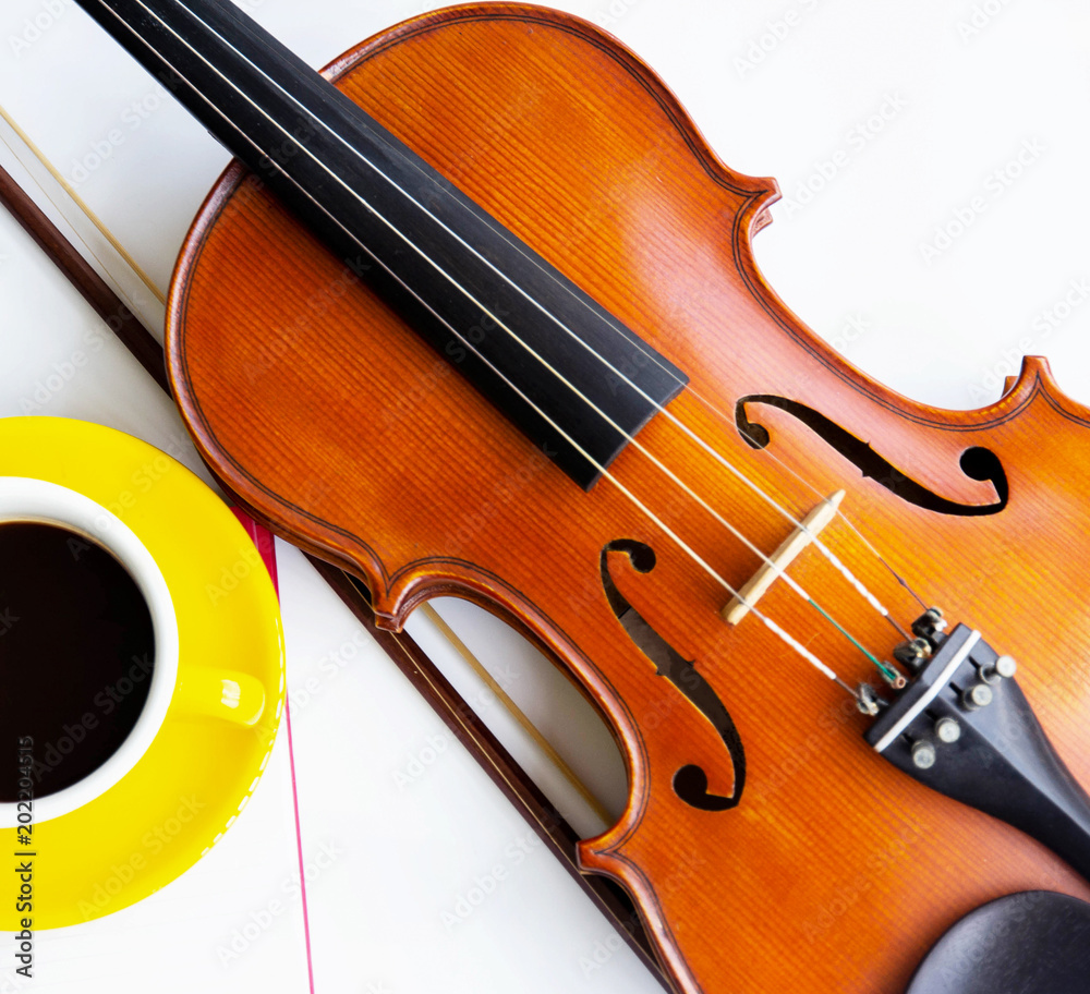 Fototapeta premium The classic violin and bow put beside half of yellow ceramic coffee cup