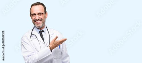 Doctor senior man, medical professional holding something in empty hand isolated over blue background photo