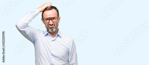 Middle age man with glasses doubt expression, confuse and wonder concept, uncertain future isolated over blue background