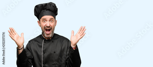 Senior cook man, wearing chef hat happy and surprised cheering expressing wow gesture isolated over blue background