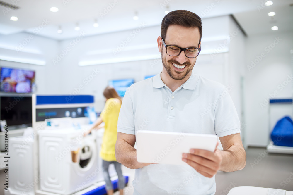 Portrait of happy satisfied young bearded man with eyeglasses testing a tablet in a tech store. Portrait of happy satisfied young bearded man with eyeglasses testing a tablet in a tech store.