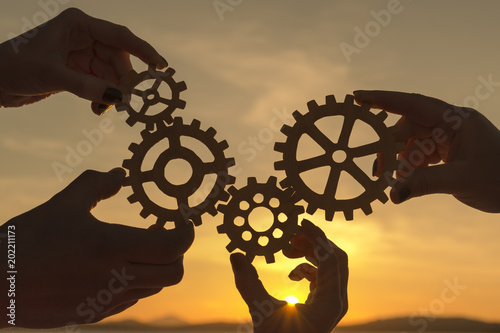 the hands of people are holding gears against the background of the evening sky. business team work.