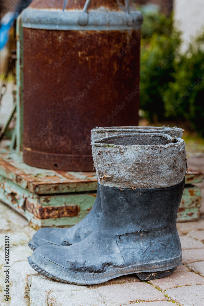 Very old wellingtons and copper bottle standing outside