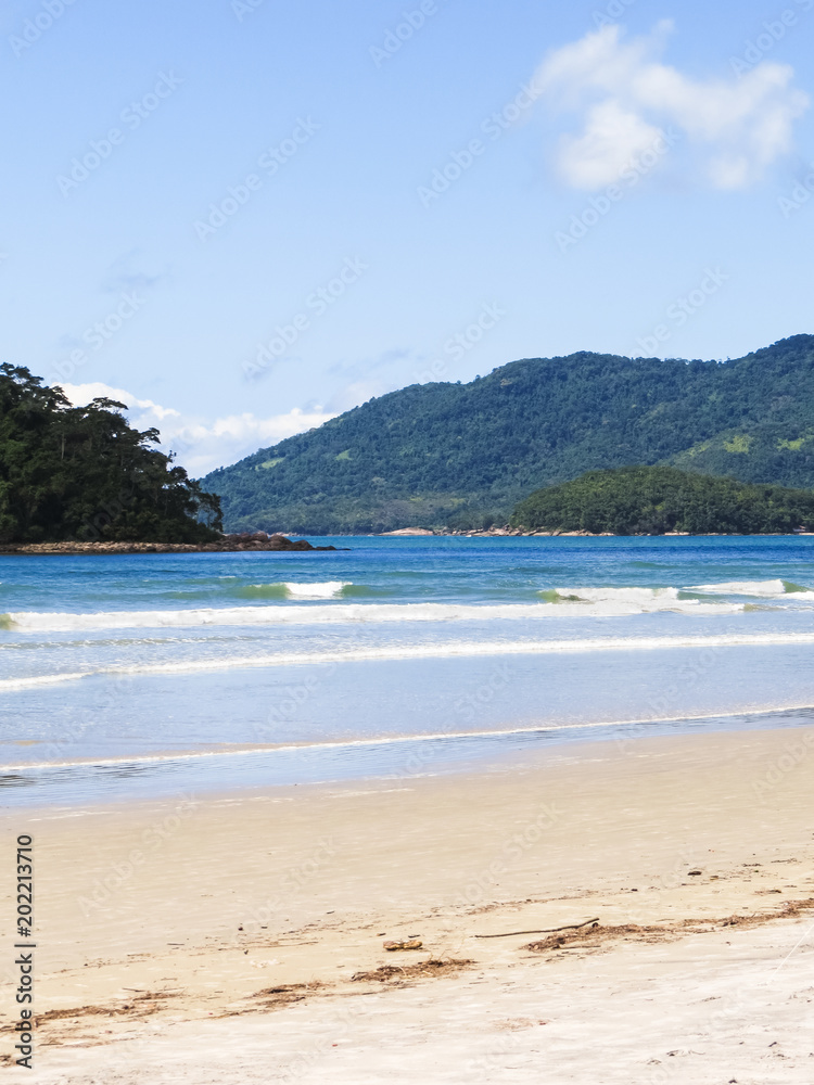 Beach in sunny day, with island and hills with forest in the background.