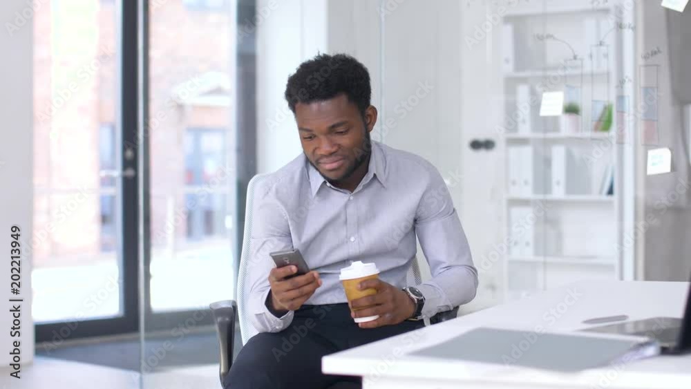 business, people and technology concept - african american businessman with smartphone having break and drinking coffee at office business, people and technology concept - african american businessman with smartphone having break and drinking coffee at office