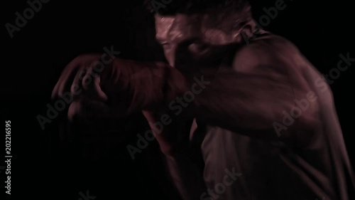 young man with fighting wrist wraps in shadow boXing workout sweaty and active on black background and extreme sport studio lighting in fitness and healthy lifestyle concept