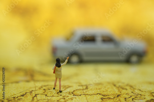 Business and Travel Concept. Businesswoman miniature figure with handbag looking and hand shake to with mini car model on world map as background.