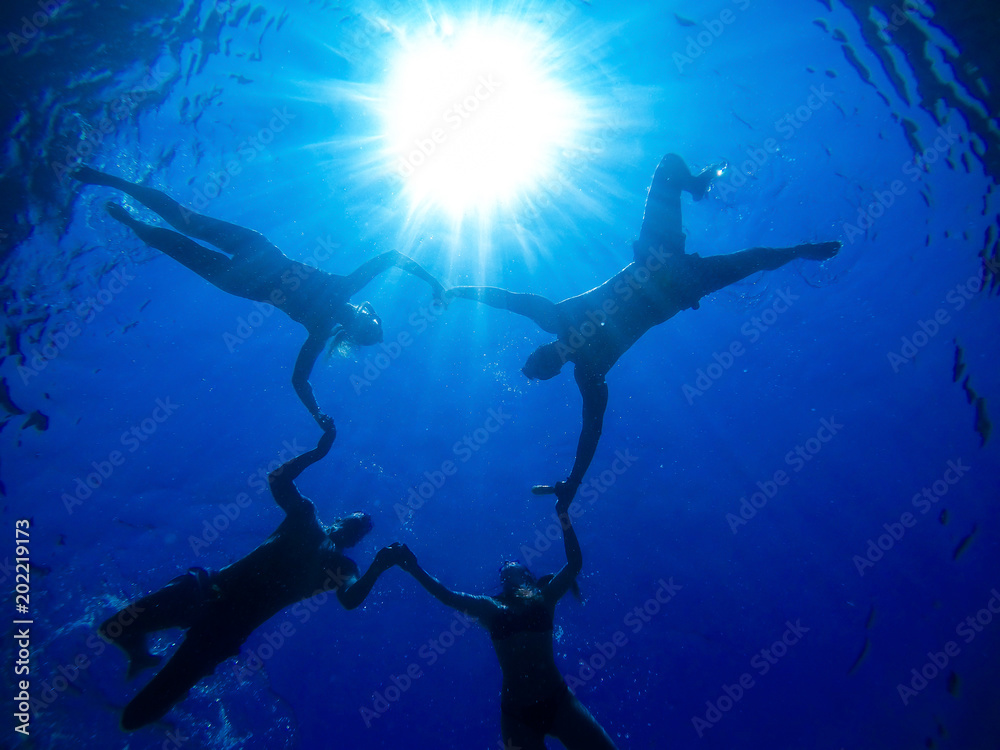 Fototapeta premium Underwater image of four playful friends enjoying holidays in the sea, holdings hands together and making star or circle.