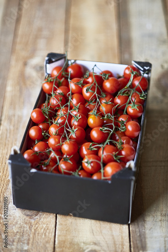 Ripe Cherry tomatoes branches in a market cardboard box over a rustic wooden table. photo