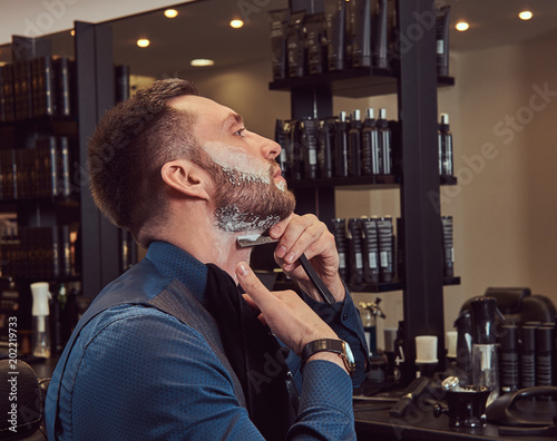 Portrait of a stylish male who himself shaving in a hairdressing salon.