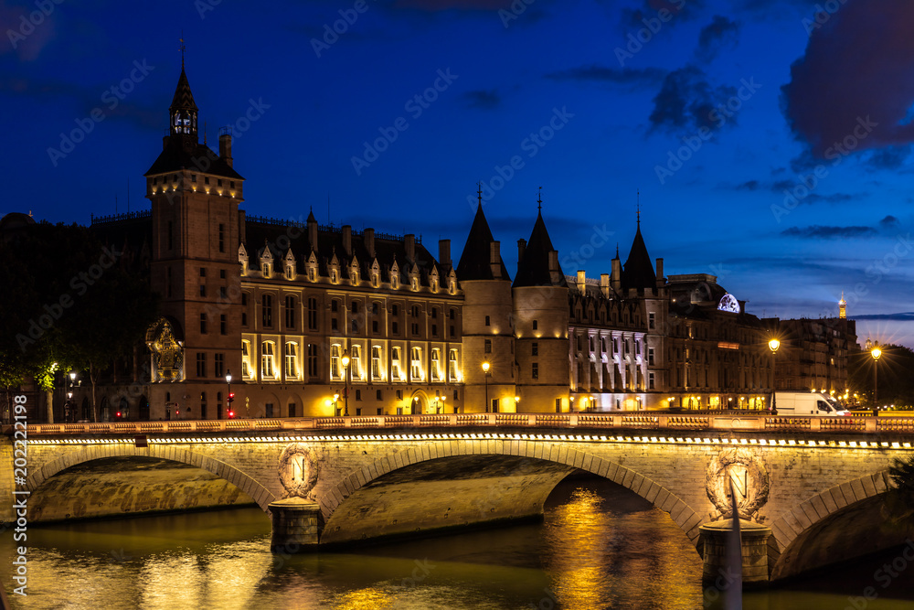 Night view of Conciergerie Castle and Bridge of Change over river Seine. Paris, France