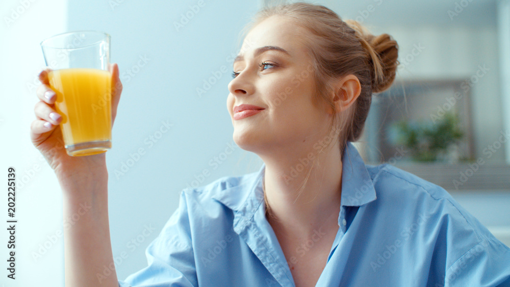 Portrait of happy young woman drinking orange juice during breakfast. - obrazy, fototapety, plakaty 