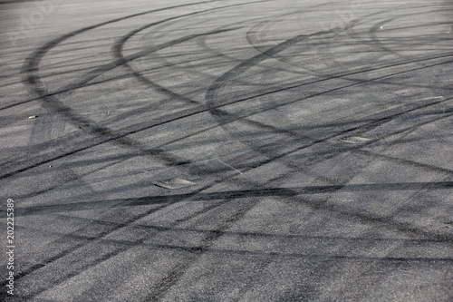 Abstract transportation background with turning black tire tracks over dark asphalt road pavement