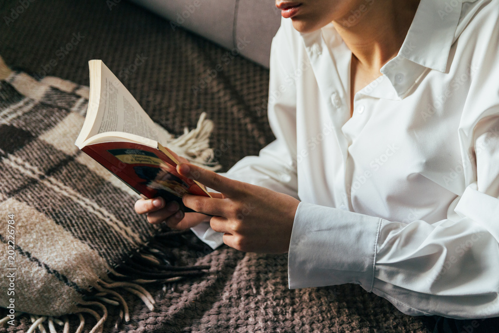 Obraz premium girl reading a book in a warm blanket. woman lies, lay down on the bed, a blanket, a sofa, a couch and holds a book. Girl reading a book