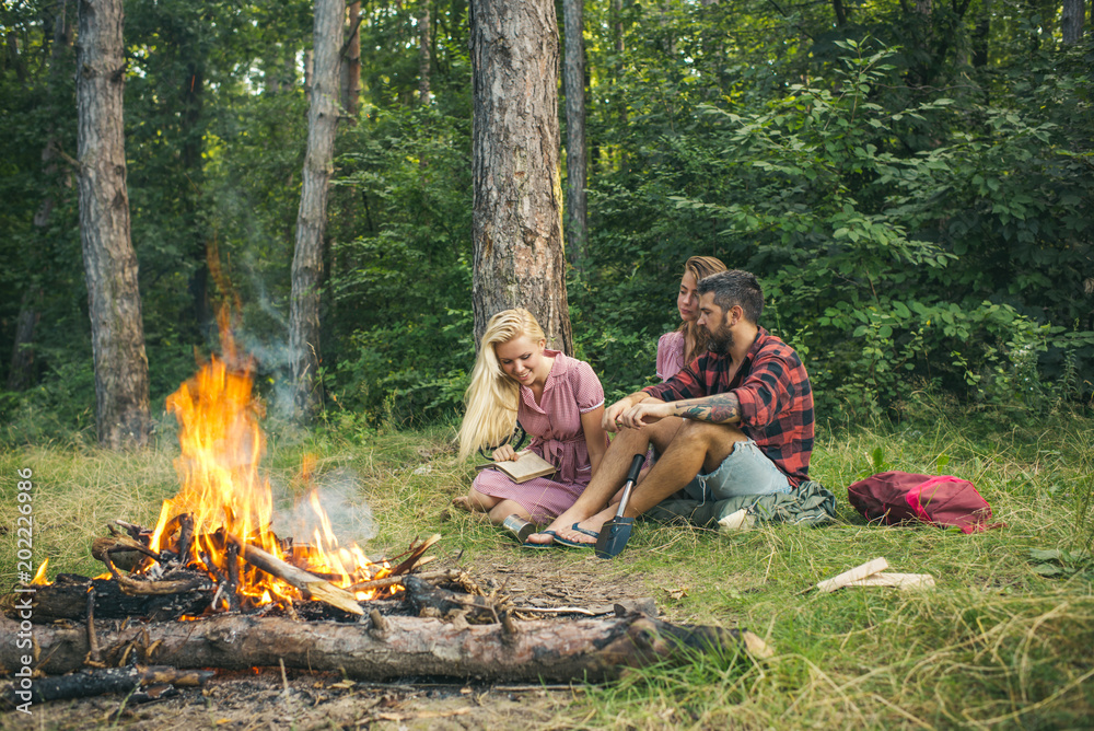 Active lifestyle concept. Group of friends camping in the forest. Girl reading next to bonfire Active lifestyle concept. Group of friends camping in the forest. Girl reading next to bonfire