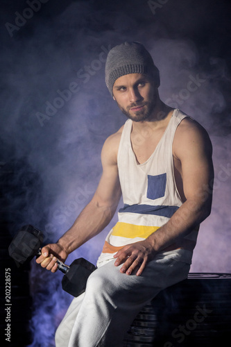 athletic handsome muscular man doing exercises with dumbbells in smoke