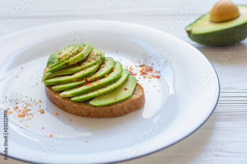 Toast with cutted avocado and spices in white plate on white wooden background. Close-up