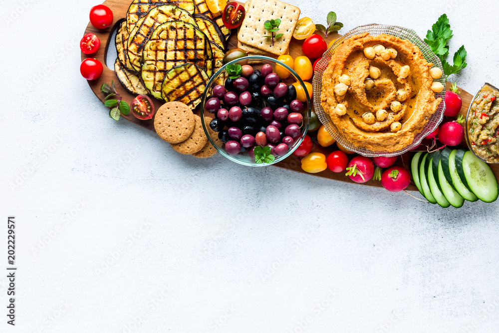 Vegan snack board. Various Vegetarian dishes  hummus with sun-dried tomatoes with crackers, aubergines grill , fresh vegetables on wooden board on white background. Clean eating, dieting food concept