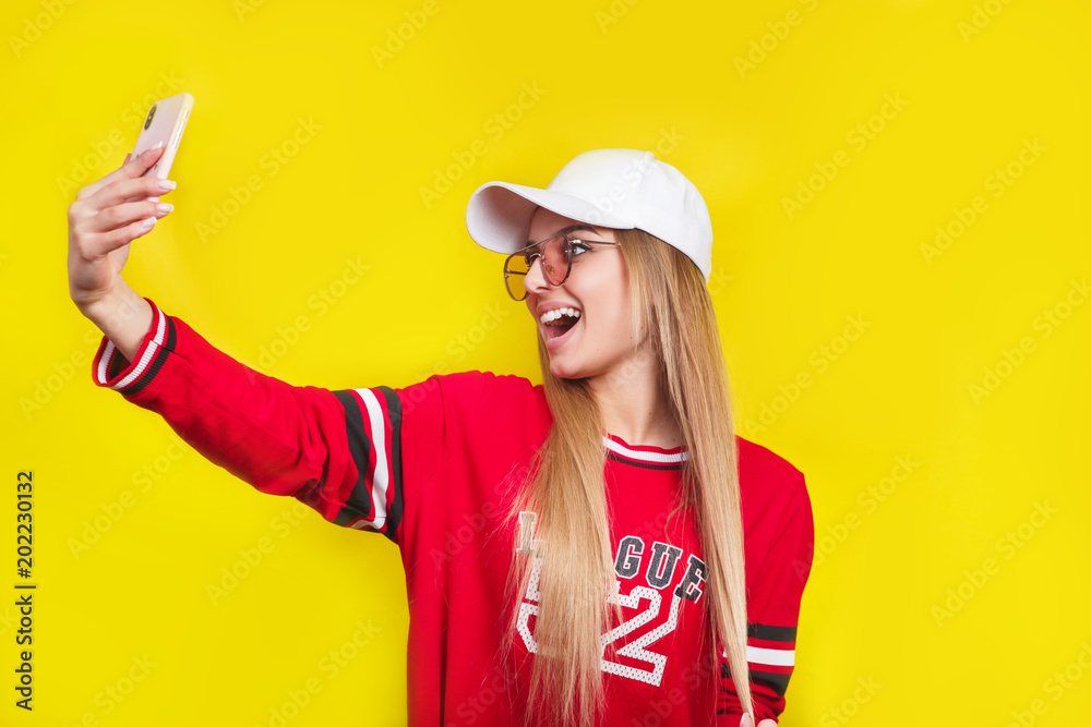 Portrait of a young attractive woman in sunglasses making selfie photo on smartphone isolated on a yellow background Portrait of a young attractive woman in sunglasses making selfie photo on smartphone isolated on a yellow background