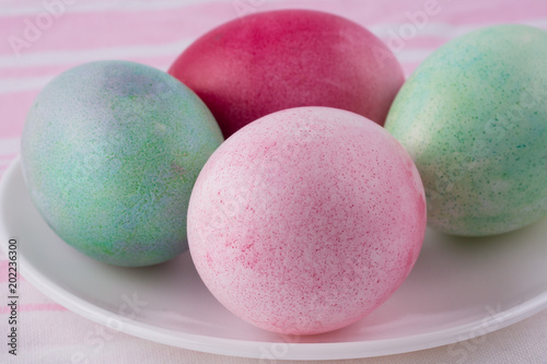 four multicolored painted Easter eggs on a white plate and striped pink-white tablecloth. holiday easter greeting card, poster, wallpaper