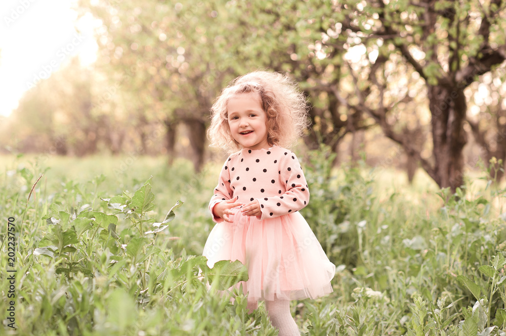 Smiling blonde kid girl 3-4 year old walking in meadow in sunny day. Happiness. Childhood.