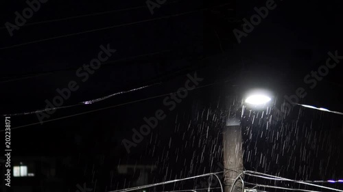 dark scene with heavy rain over electric post with thunderstrike light at background