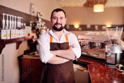 portrait of a handsome male barista in an apron on the background of a cozy coffee house and a coffee machine.
