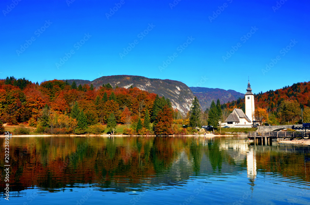 Typical view of the Bohinj lake with a church and autumn fall trees reflected in water, Slovenia