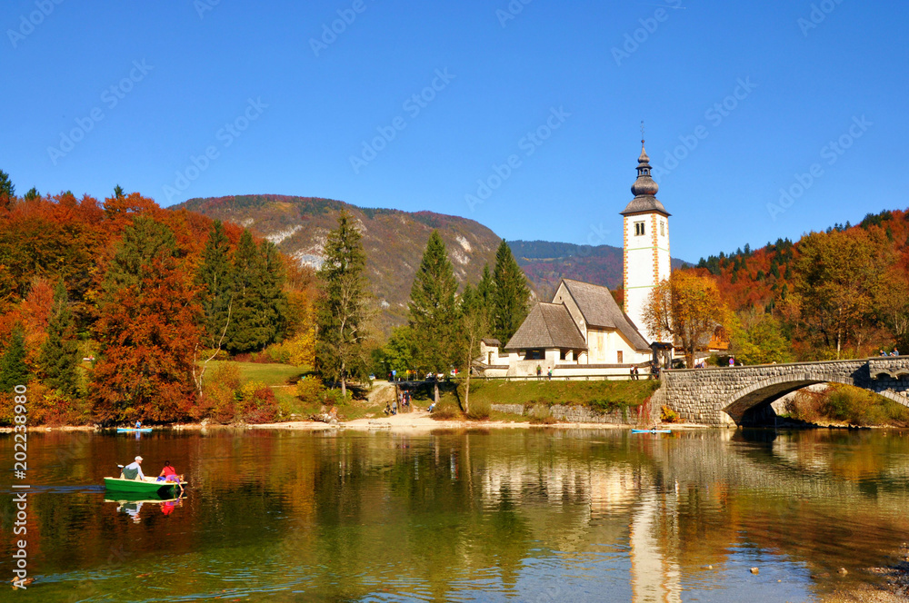 Typical view of the Bohinj lake with a St. John church and autumn trees reflected in water, Slovenia