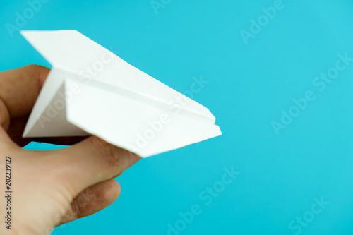 Hand holding paper airplane on light blue background.
