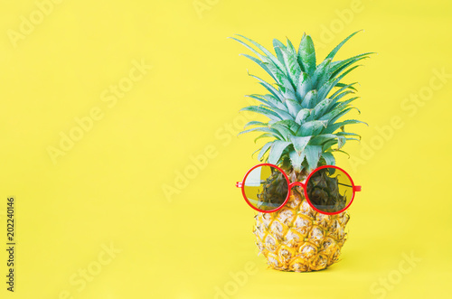 Pineapple with red sunglasses on yellow background - Summer background