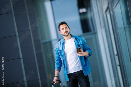 young businessman walking through the financial district of the city with his smartphone and suitcase. business concept photo