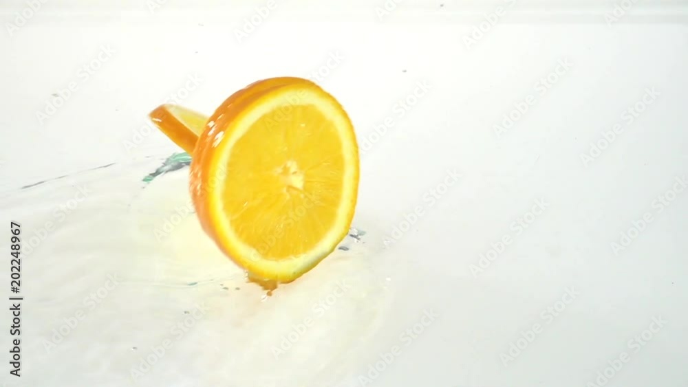 Part of the orange drops into the water . White background. Slow motion Part of the orange drops into the water . White background. Slow motion