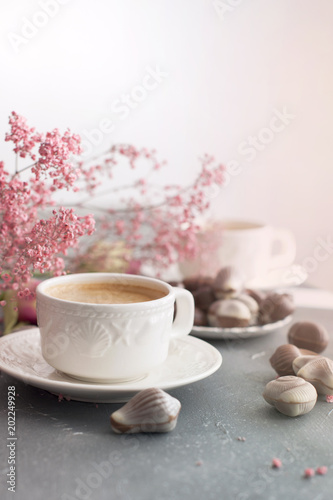 Chocolate sweets in the form of cockleshells and two cups of fragrant coffee. Romantic breakfast. Light colors. Pink flowers. Free space for text