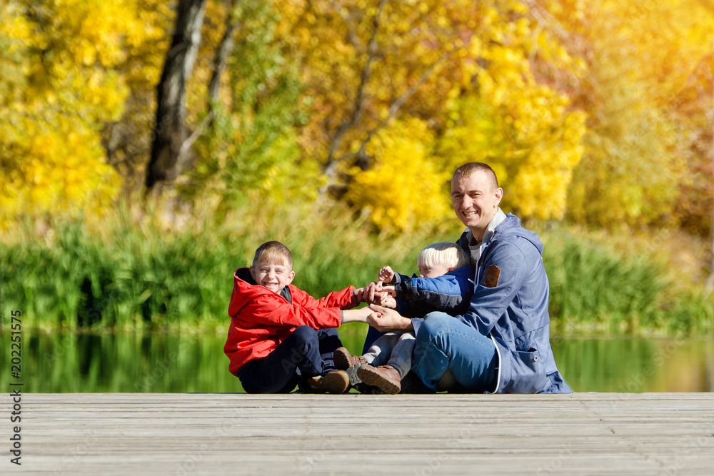 Father and two sons play on the dock. Autumn, sunny. Side view