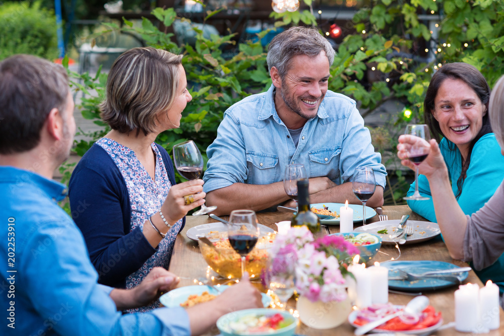 Beautiful summer evening in the garden, a group of friends in their forties have a good time laughing together around a table. Beautiful summer evening in the garden, a group of friends in their forties have a good time laughing together around a table.