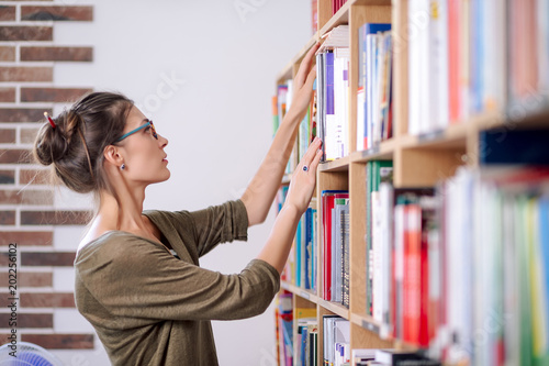 Young woman wearing glasses looking for a book on a bookshelf, i photo