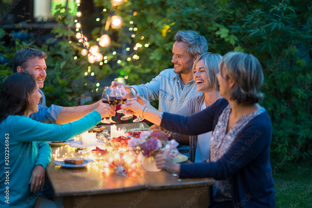 Fotografie One summer evening, friends in their forties gathered around a table in the garden lit by luminous garlands
