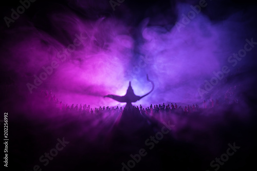 Lamp of wishes. Silhouette of a large crowd of people standing against a big lamp of wishes with toned light beams on foggy background. Dark night table decoration.