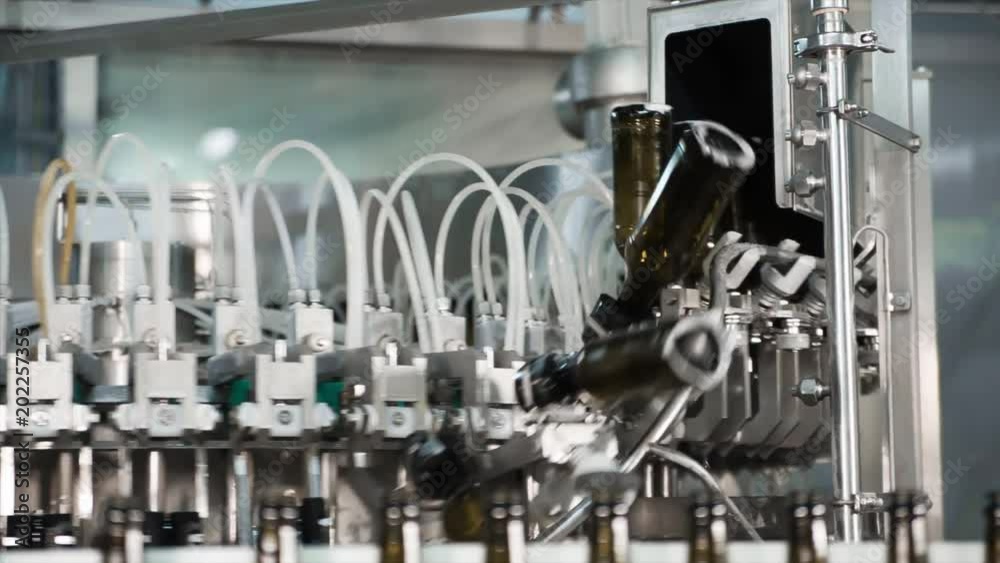Automatic filling machine pouring beer in a brewery. Glass bottles for beer on the conveyor belt. Filling machine for industry. Automatic filling machine pouring beer in a brewery. Glass bottles for beer on the conveyor belt. Filling machine for industry.