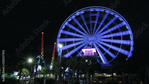 Time lapse of Ferris Wheel at night with muti-colored lights and stars moving across the night sky photo