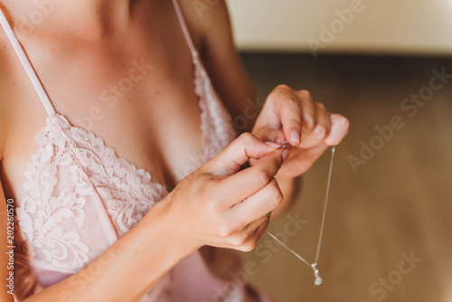 Young woman in beautiful pink lingerie unfastening a delicate necklace