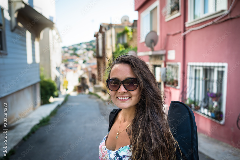 Young woman with case for a musical instrument on the back stands on the city street and smiling. Pretty girl traveler with violin. Young woman with case for a musical instrument on the back stands on the city street and smiling. Pretty girl traveler with violin.