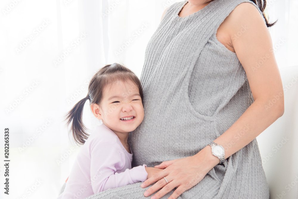 Little asian girl listening sound from her pregnant mother's belly and smiles